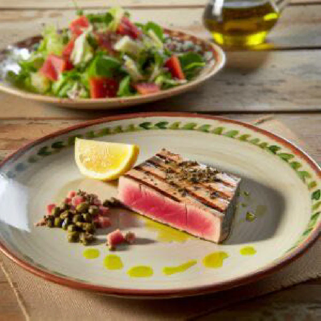 Grilled tuna steak with lemon and fresh herbs on a white plate