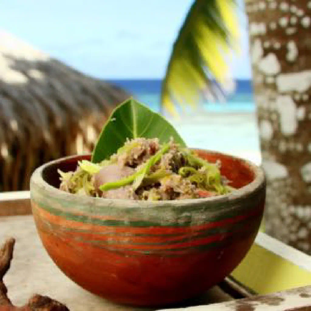 Bowl of Kuti with cubed raw fish, mango and coconut milk garnished with fresh herbs