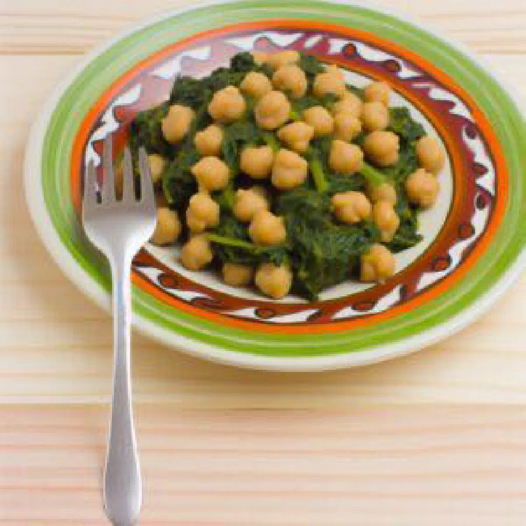 A bowl of chickpeas and wilted spinach garnished with fresh herbs