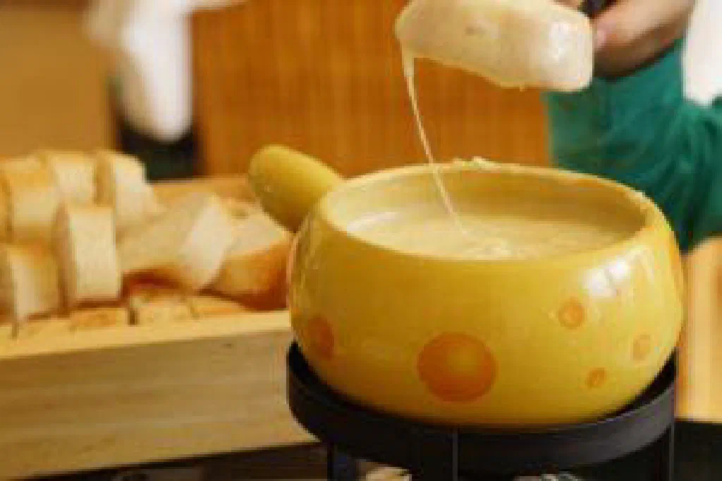 Melted cheese fondue in a caquelon with cubes of bread on forks