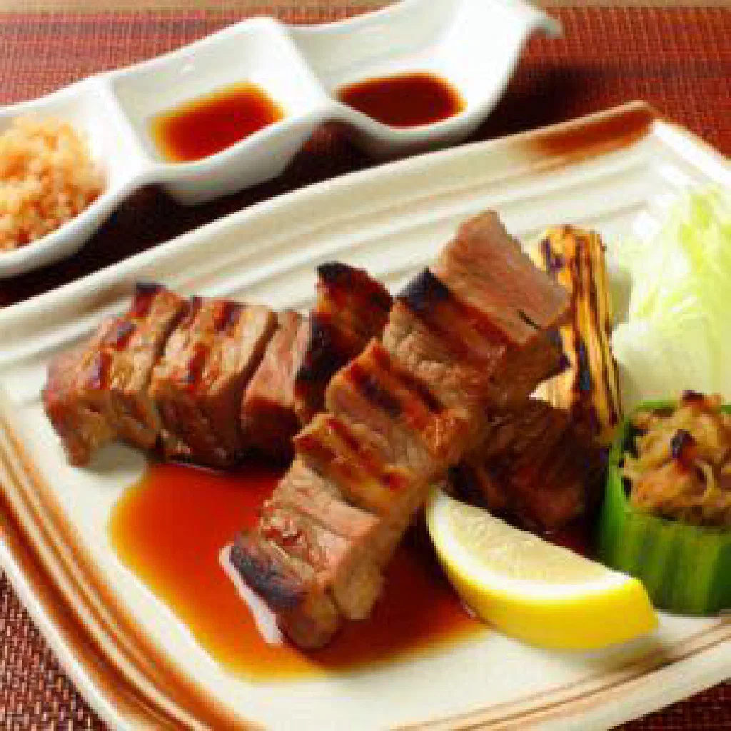 Grilled nyama choma meat on a wooden board with lemon wedges