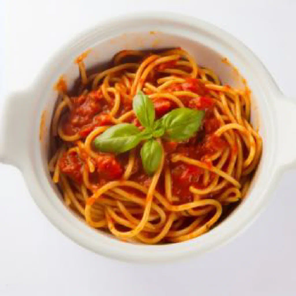 A bowl of spaghetti coated in rich tomato tuco sauce, garnished with fresh basil