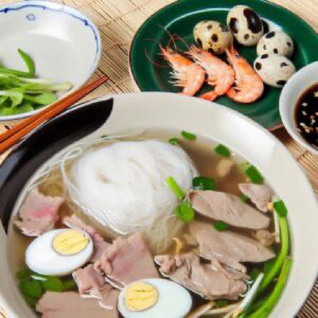 Bowl of Hu Tieu noodle soup with pork, prawns and fresh herbs